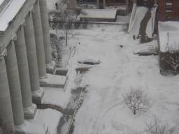 A snowed under car next to a building with huge pillars