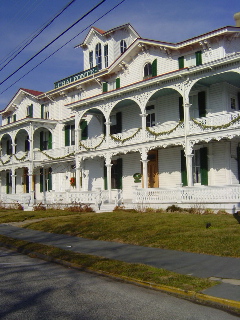 A fancy antique hotel building with ornate porches that are decorated with christmas greens. The building has white siding and a red roof and a sign that says CHALETONTE. 