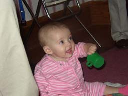 Baby Claire smiles and holds a green cup in her little hand
